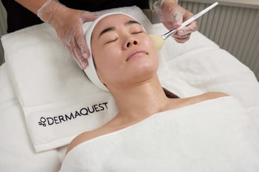 Image of woman in a DermaQuest professional treatment chemical peel getting product applied on her skin with a fan brush
