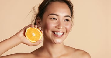 Smiling woman with radiant face skin holding orange in hand