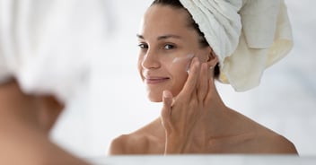 Young woman looking into mirror and applying face cream
