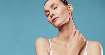 serene woman with glowing skin and closed eyes gently touching her neck against a blue background