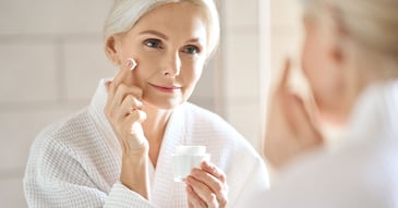 woman applying cream to face in bathroom