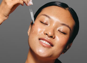 Close up of woman with healthy skin applying serum to her skin with a dropper and smiling