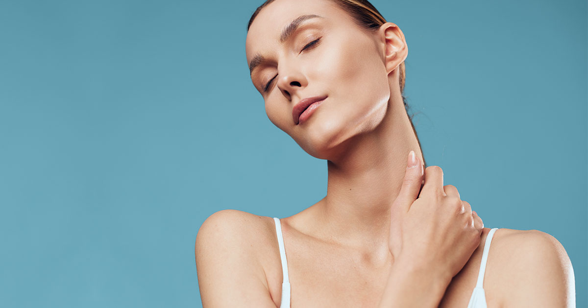 serene woman with glowing skin and closed eyes gently touching her neck against a blue background